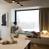 Un coin lecture scandinave parfait pour admirer la neige. Une femme savoure une boisson chaude, enveloppée dans un plaid douillet.
