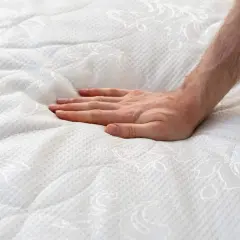 Main d'une personne appuyant sur un matelas blanc, créant une empreinte. Est-ce normal que mon matelas neuf se creuse ?