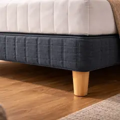 Un lit avec un sommier bleu foncé capitonné et des pieds en bois coniques. La hauteur du lit est celle d'un hauteur lit standard.
