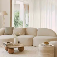 Salon lumineux avec canapé arrondi, table basse organique et pouf texturé. Une ambiance de deco epuree chic, invitant à la détente.