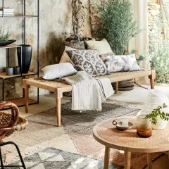 Un canapé moche en corde tressée, orné de coussins décoratifs, dans un salon bohème avec des plantes et une lumière douce.