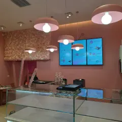 Cinq luminaires identiques, de couleur rose, éclairent un salon de thé aux murs ornés de fleurs roses.
