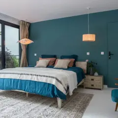 Chambre bleu nuit et bois, avec un grand lit douillet, une fenêtre donnant sur la verdure et une touche de naturel.