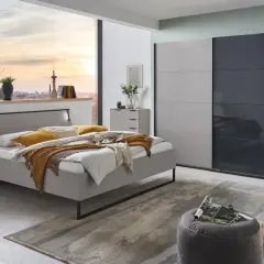 Chambre grise cocooning avec lit douillet, armoire moderne et vue sur la ville au coucher du soleil.