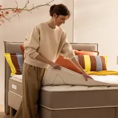 Une femme ajuste un surmatelas sur un lit. Idéal pour savoir comment surélever un lit et améliorer le confort.