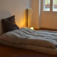 Un matelas au sol sans sommier, prêt pour une nuit paisible. Une bougie allumée éclaire doucement la pièce.