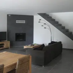 Salon moderne avec mur noir autour de la cheminée, sol gris foncé, escalier en béton, canapé marron et meuble TV en bois. Quelle couleur de mur avec un sol gris foncé ? Le noir contraste bien.