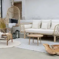 Salon avec une ambiance deco boheme chic. Fauteuil en rotin, canapé blanc, table basse en bois, et un fauteuil suspendu.