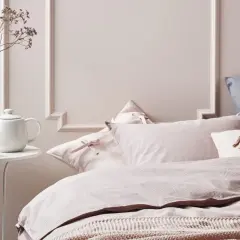 Chambre couleur pastel mur avec un lit douillet, des coussins roses à rayures et une théière blanche sur une table.