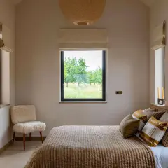 Une petite chambre parentale cosy avec un lit douillet, un fauteuil en peau de mouton et une vue sur la nature.