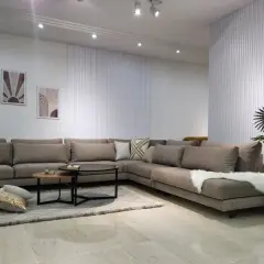 Un grand canapé d'angle taupe, parfait pour réfléchir à quelle couleur de canapé choisir. Décoration murale et plante verte complètent l'ensemble.