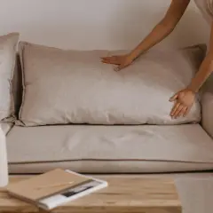 Comment faire pour le rembourrage canapé coussins avachis ? Une main ajuste un coussin pour lui redonner sa forme.