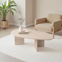 Table basse ovale en travertin, avec une plante verte et un fauteuil en tissu beige.