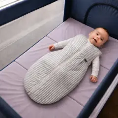 Bébé souriant dans un lit parapluie, sur un matelas adapté. La taille du matelas lit parapluie est parfaite pour le confort de bébé.
