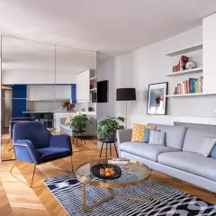 Salon moderne avec canapé gris, fauteuil bleu, table basse ronde et parquet. La deco petit appartement moderne est lumineuse et élégante.