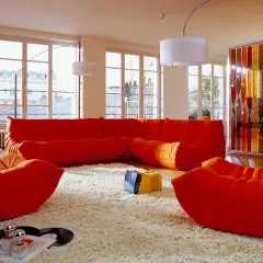 Salon aux couleurs vives, mobilier années 70 caractéristiques : canapé orange, fauteuils Togo, tapis shaggy, écran décoratif coloré.