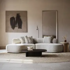 Un **salon écru** aux lignes douces, avec un canapé arrondi, un tapis rond en jonc de mer et une œuvre d'art abstraite.