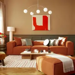 Salon cosy aux tons terreux. Un canapé orange vif, des coussins doux et une peinture abstraite rouge créent une ambiance chaleureuse. La **couleur chaude peinture** domine, invitant à la détente.