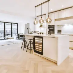 Éclairage cuisine ouverte sur salon avec îlot central, cave à vin et tabourets. Lumière douce et moderne.