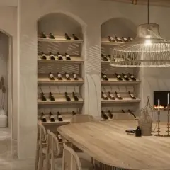 Salle à manger chaleureuse avec une grande table en bois, des étagères à vin remplies, une cheminée et une ambiance deco boho chic.
