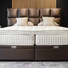 Un lit moderne avec un sommier capitonné marron, idéal pour poser un sommier à lattes. Le matelas est blanc et deux coussins décoratifs sont présents.