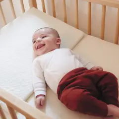 Un bébé souriant dans un lit en bois. Quel lit pour bébé est le plus confortable ? Ce matelas semble parfait pour des siestes douces.
