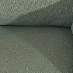 Gros plan sur le tissu texturé d'un canapé vert. Une assise de canapé qui glisse, créant une ombre douce.