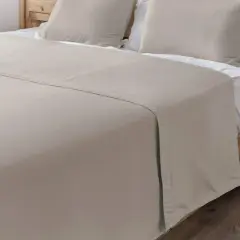 Un drap de lit beige, taille 140x190, est posé sur un lit en bois avec des oreillers assortis.