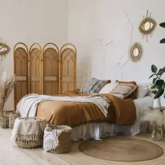 Une chambre d'amis cosy avec un lit douillet, des paniers en osier, des miroirs soleil et une plante verte luxuriante.