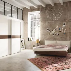 Chambre moderne avec grand placard blanc, lit bas, tapis oriental et mur en béton. Une décoration murale de photos et une lampe originale complètent ce **feng shui chambre**.