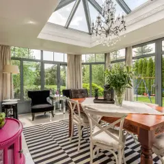 Veranda salon cocooning avec table en bois, lustre en cristal et vue sur jardin verdoyant.