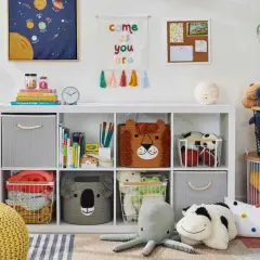 Idée petite chambre bébé : étagère blanche remplie de jouets, paniers animaux, coussins, et décorations murales colorées.