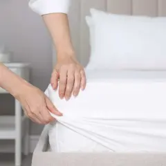 Mains ajustant un drap housse blanc sur un matelas. La question est : quelle taille de drap housse pour un lit 160x200 ?