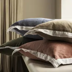 Pile de coussins aux couleurs douces, en matière drap de lin, avec des bordures blanches.