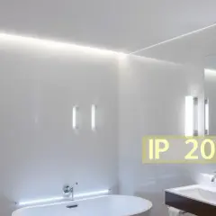 Salle de bain moderne avec baignoire, lavabo et miroir. L'éclairage subtil met en valeur le design épuré. Le texte "IP 20 signification" indique la protection contre les corps solides.