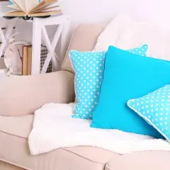 Un plaid blanc moelleux est disposé sur un canapé beige, orné de coussins bleus vifs et à pois. Idéal pour savoir comment disposer un plaid sur un canapé.