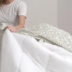 Une personne en t-shirt blanc commence à mettre la housse de couette à motifs feuilles sur une couette blanche.