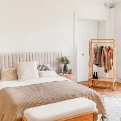 Chambre bohème scandinave avec lit douillet, table de chevet en bois, portant à vêtements en rotin et fenêtre lumineuse.