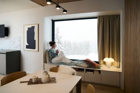 Un coin lecture scandinave parfait pour admirer la neige. Une femme savoure une boisson chaude, enveloppée dans un plaid douillet.