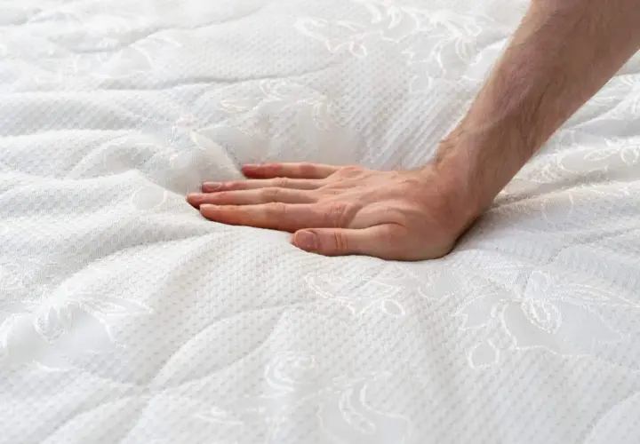Main d'une personne appuyant sur un matelas blanc, créant une empreinte. Est-ce normal que mon matelas neuf se creuse ?
