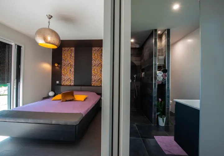 Chambre moderne avec lit violet et salle de bain attenante. La **taille suite parentale** est idéale pour un confort optimal.