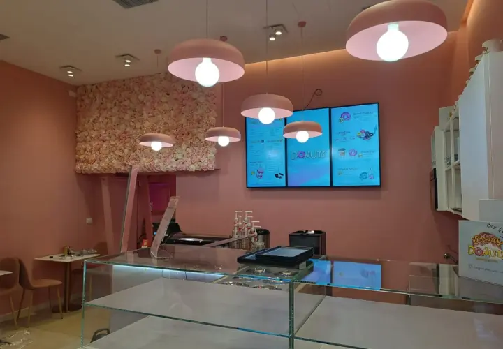 Cinq luminaires identiques, de couleur rose, éclairent un salon de thé aux murs ornés de fleurs roses.