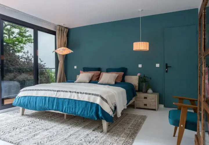 Chambre bleu nuit et bois, avec un grand lit douillet, une fenêtre donnant sur la verdure et une touche de naturel.