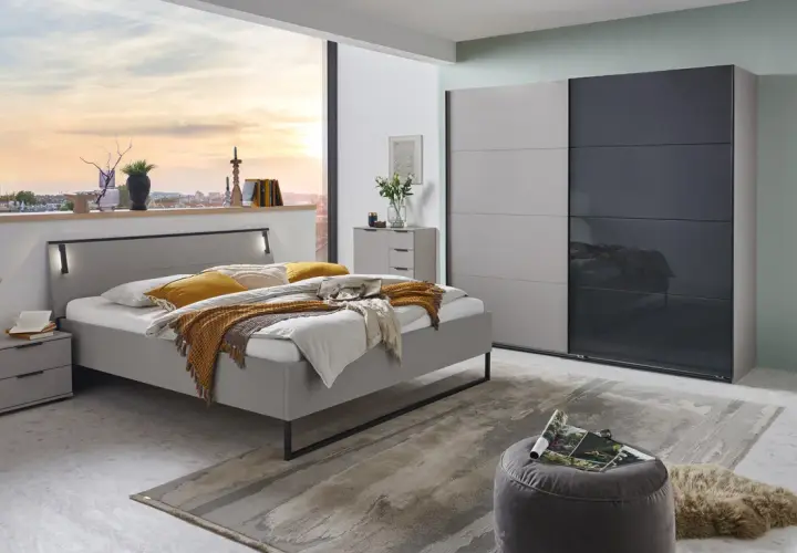 Chambre grise cocooning avec lit douillet, armoire moderne et vue sur la ville au coucher du soleil.