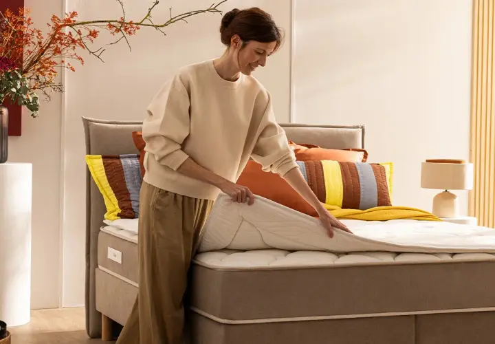 Une femme ajuste un surmatelas sur un lit. Idéal pour savoir comment surélever un lit et améliorer le confort.