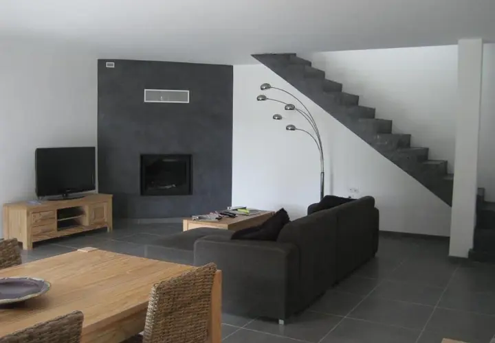 Salon moderne avec mur noir autour de la cheminée, sol gris foncé, escalier en béton, canapé marron et meuble TV en bois. Quelle couleur de mur avec un sol gris foncé ? Le noir contraste bien.