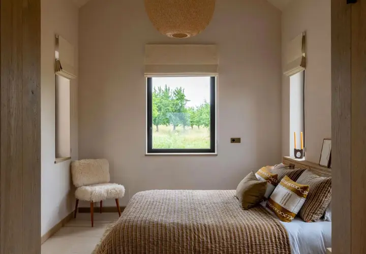 Une petite chambre parentale cosy avec un lit douillet, un fauteuil en peau de mouton et une vue sur la nature.