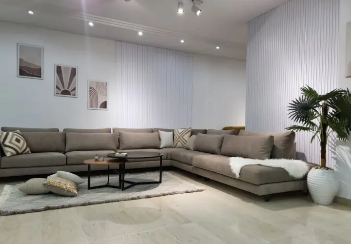Un grand canapé d'angle taupe, parfait pour réfléchir à quelle couleur de canapé choisir. Décoration murale et plante verte complètent l'ensemble.