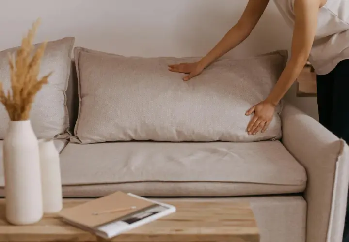 Comment faire pour le rembourrage canapé coussins avachis ? Une main ajuste un coussin pour lui redonner sa forme.