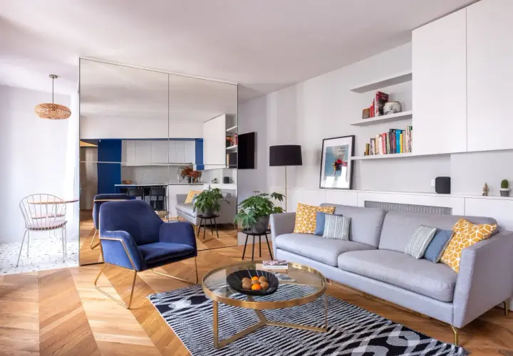 Salon moderne avec canapé gris, fauteuil bleu, table basse ronde et parquet. La deco petit appartement moderne est lumineuse et élégante.